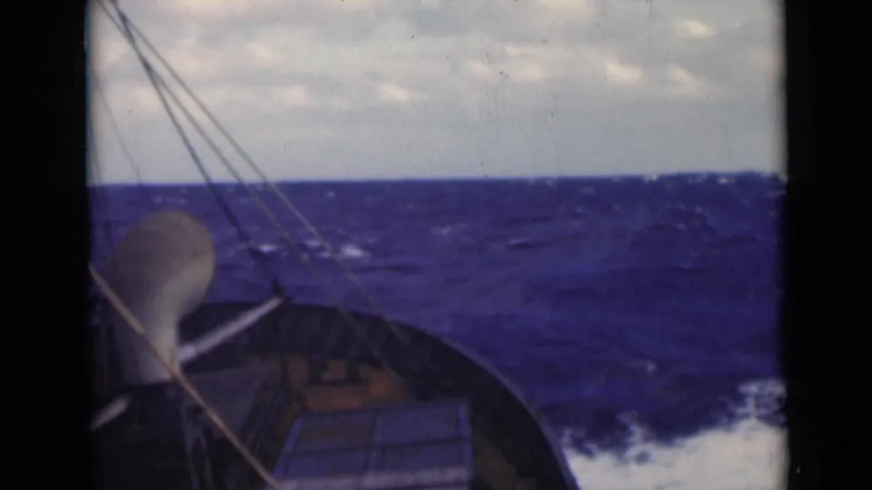 The sailboat bow and rigging remain in view as the vessel moves through rough blue water with whitecaps on the horizon.
