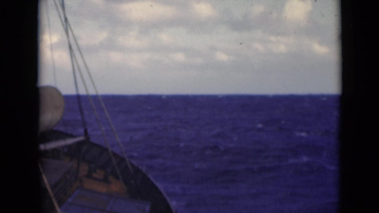 Boat bow and rigging lines facing choppy blue sea under a cloudy sky.