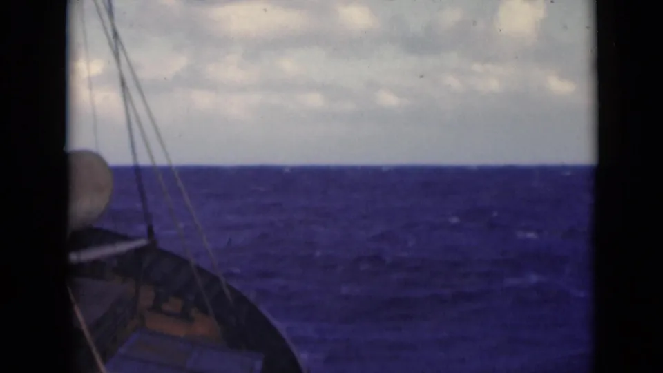 1947 8mm home-movie frame showing a boat bow at the edge of choppy blue water in the Persian Gulf, with rigging lines and a cloudy horizon.