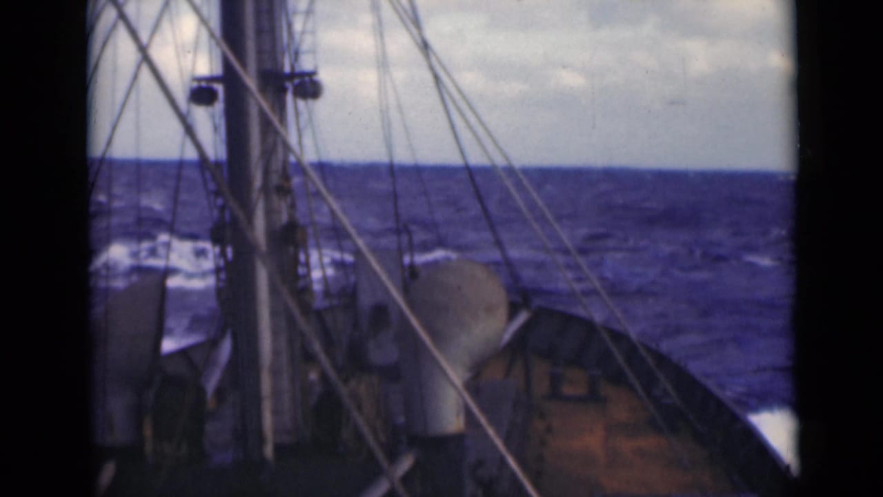 Mast, rigging, and deck fittings on a ship moving through rough water.