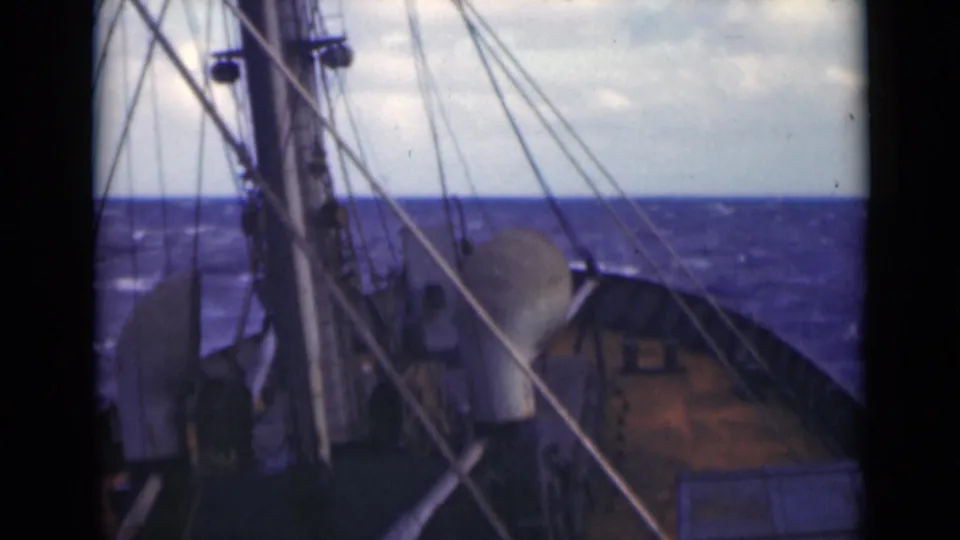 The vessel appears to bob as the forward deck, mast, and diagonal rigging lines fill the foreground against a rolling blue sea.