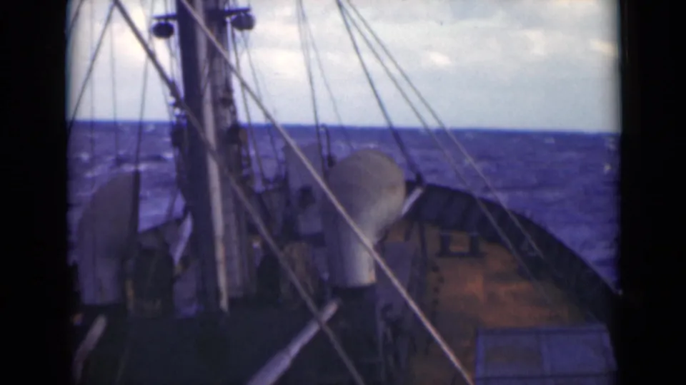 Forward-looking deck footage shows the ship bow, rigging, and pale dome-like fitting as the vessel continues across choppy open water.