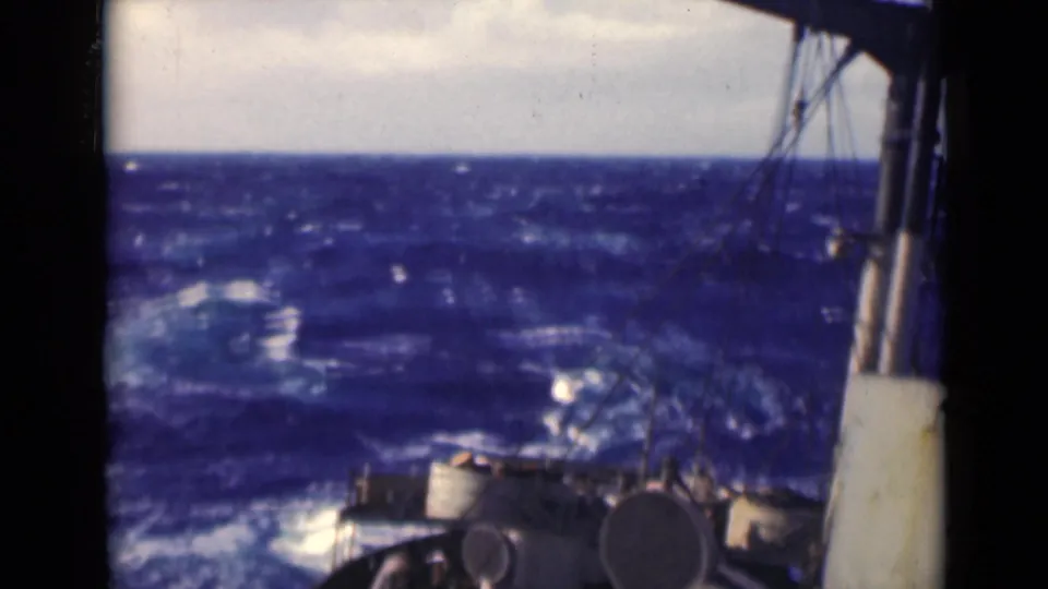 A tilted shipboard view shows the bow and rigging against rough open water, with bright whitecaps catching light across the sea.