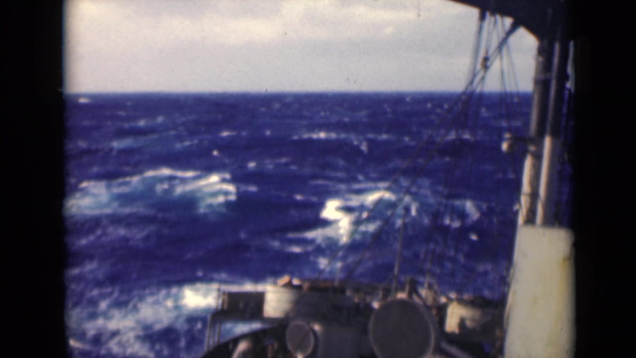Rough blue sea and whitecaps seen over a vessel deck with railings and equipment.