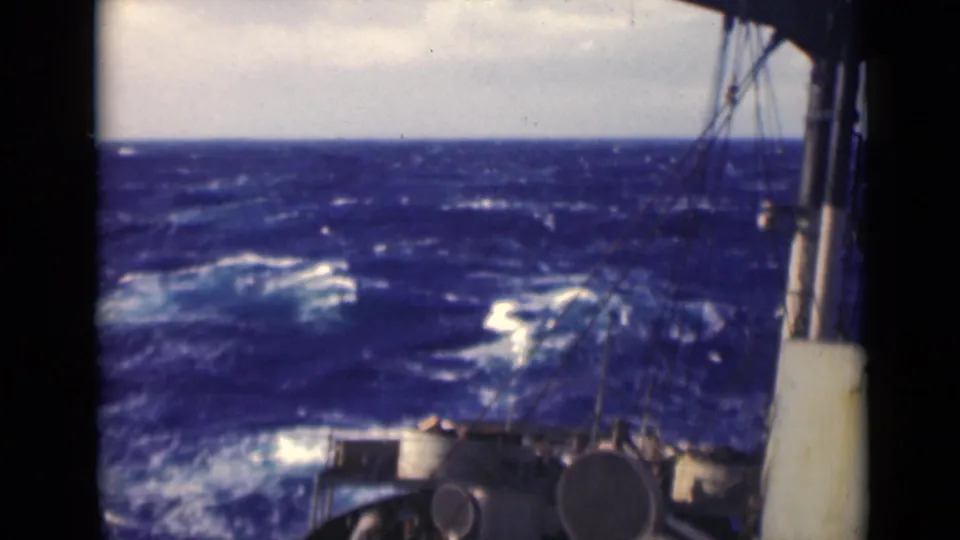 1947 8mm deck view of rough open water with whitecaps, cloudy sky, and ship equipment in the foreground.
