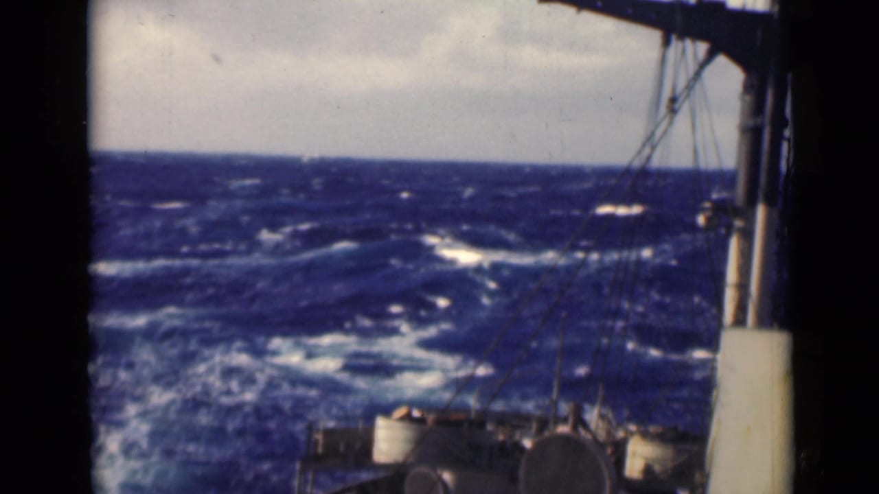Open sea with whitecaps beyond a ship deck and vertical mast structure.