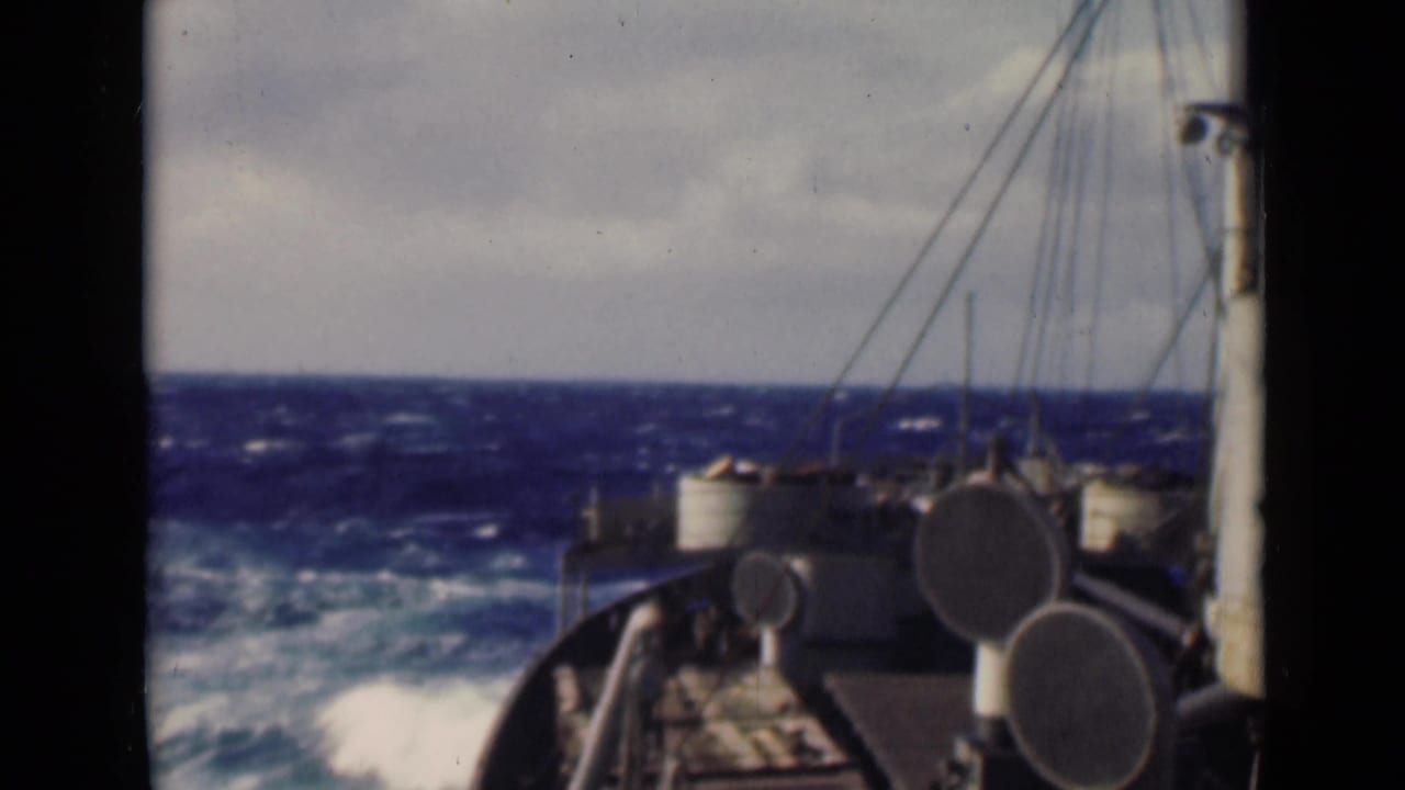 A fixed 8mm view from a ship deck shows the bow, circular ventilators, rigging, and rough blue water with white foam near the hull.