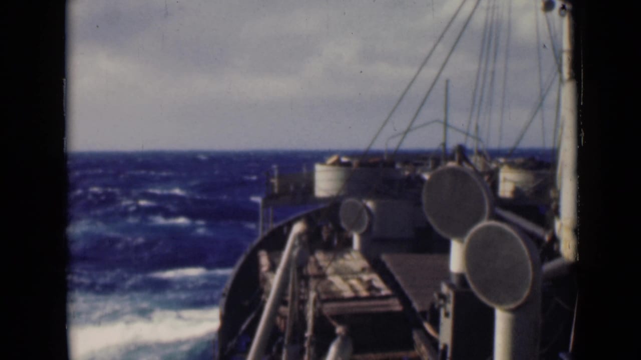 The vessel's forward deck, rail edges, circular vents, rigging, and a dark blue choppy sea are visible from a fixed onboard perspective.