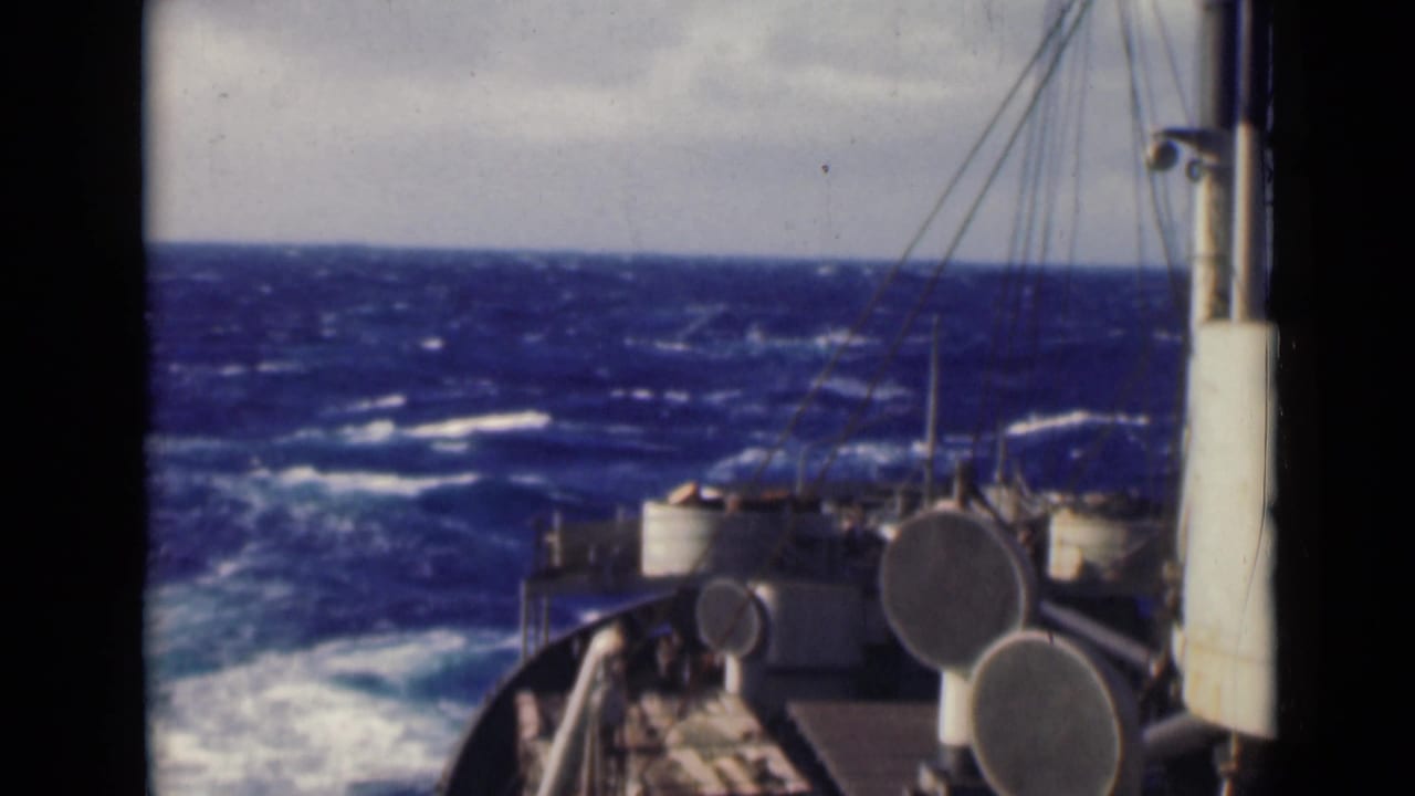 Ship bow and deck equipment facing rough blue water under a cloudy sky.