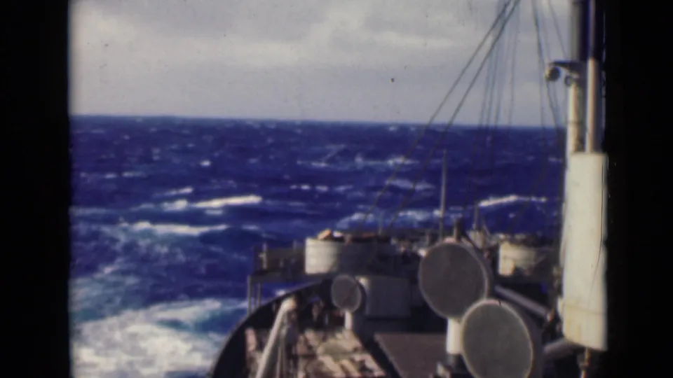 1947 8mm frame of a ship moving through rough open water, with bow railings, deck fittings, rigging, and whitecaps visible.