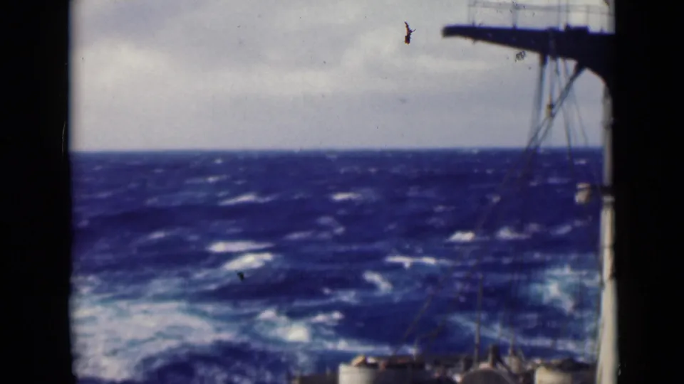 8mm frame showing rough open water and part of the vessel's deck, with rigging and a vertical deck structure at the edge of the shot.