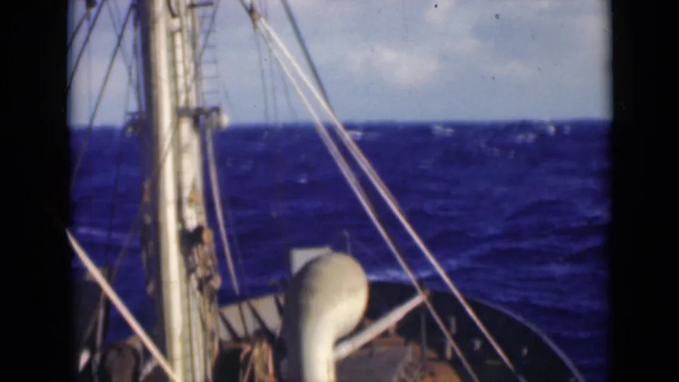 Deck-level 8mm view of a ship moving through choppy water, with mast and rigging on the left.