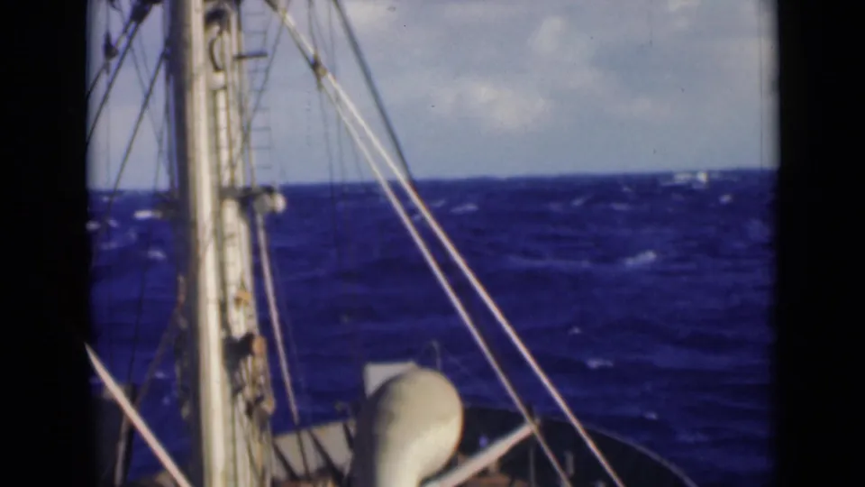 1947 8mm maritime frame with ship rigging, bow edge, and rough blue sea under a pale cloudy sky.
