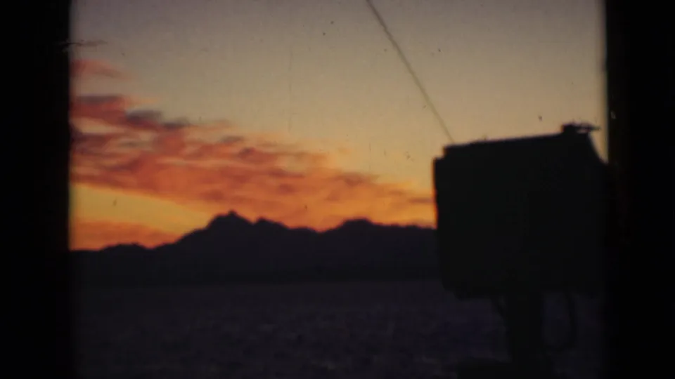 A warm orange-pink sky glows above a dark mountain horizon, with an indistinct silhouetted object in the foreground.
