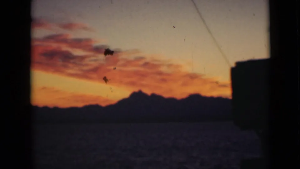 A saturated dawn or dusk sky appears above a dark mountain range, with a black foreground shape along the right edge.