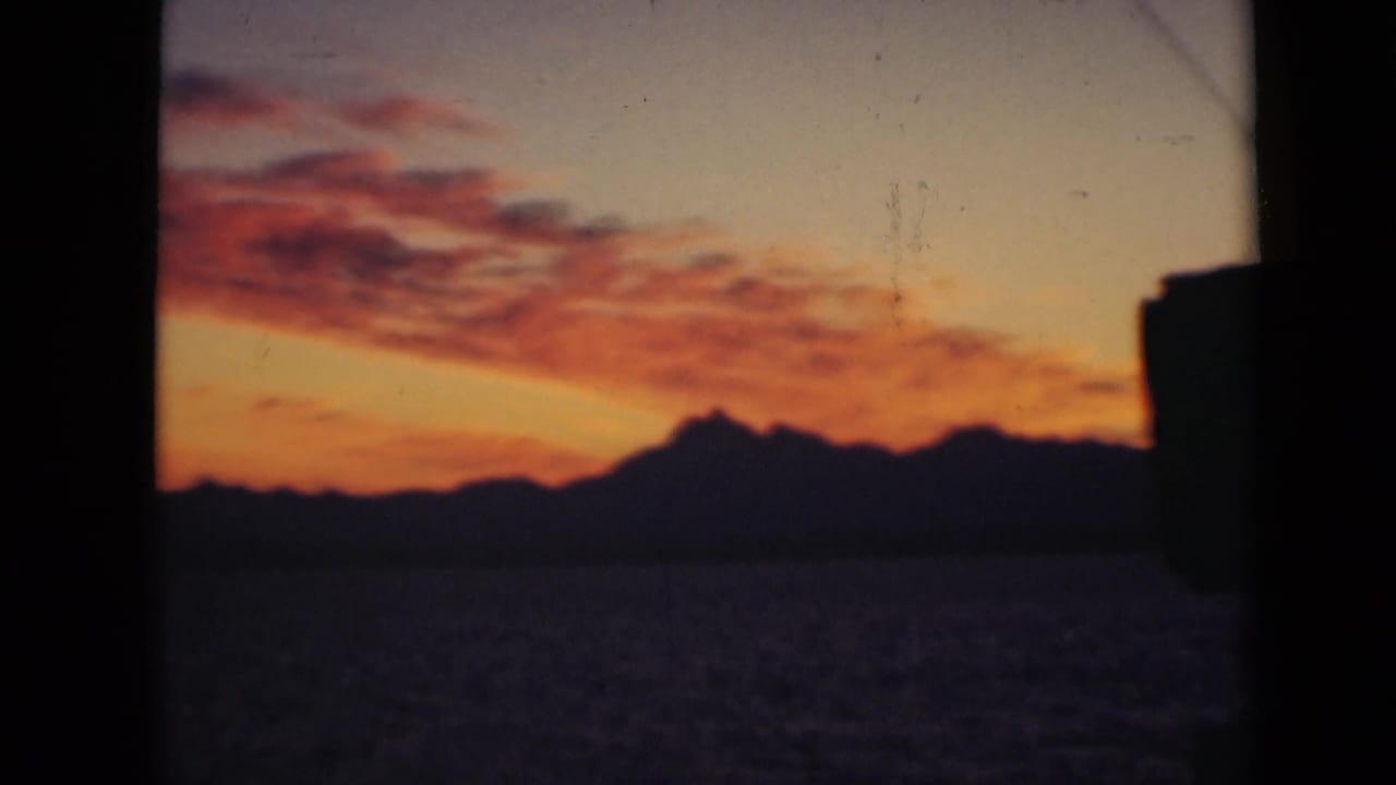 Sunset sky over dark water and a silhouetted horizon, seen through a window frame.