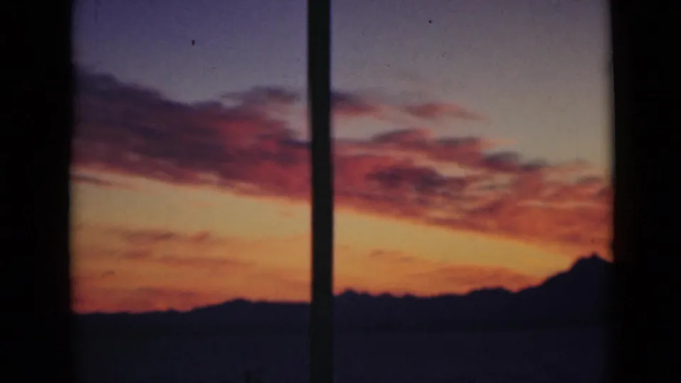 Short 8mm-style sunset view with red clouds, dark water, and a silhouetted horizon divided by a vertical window bar.