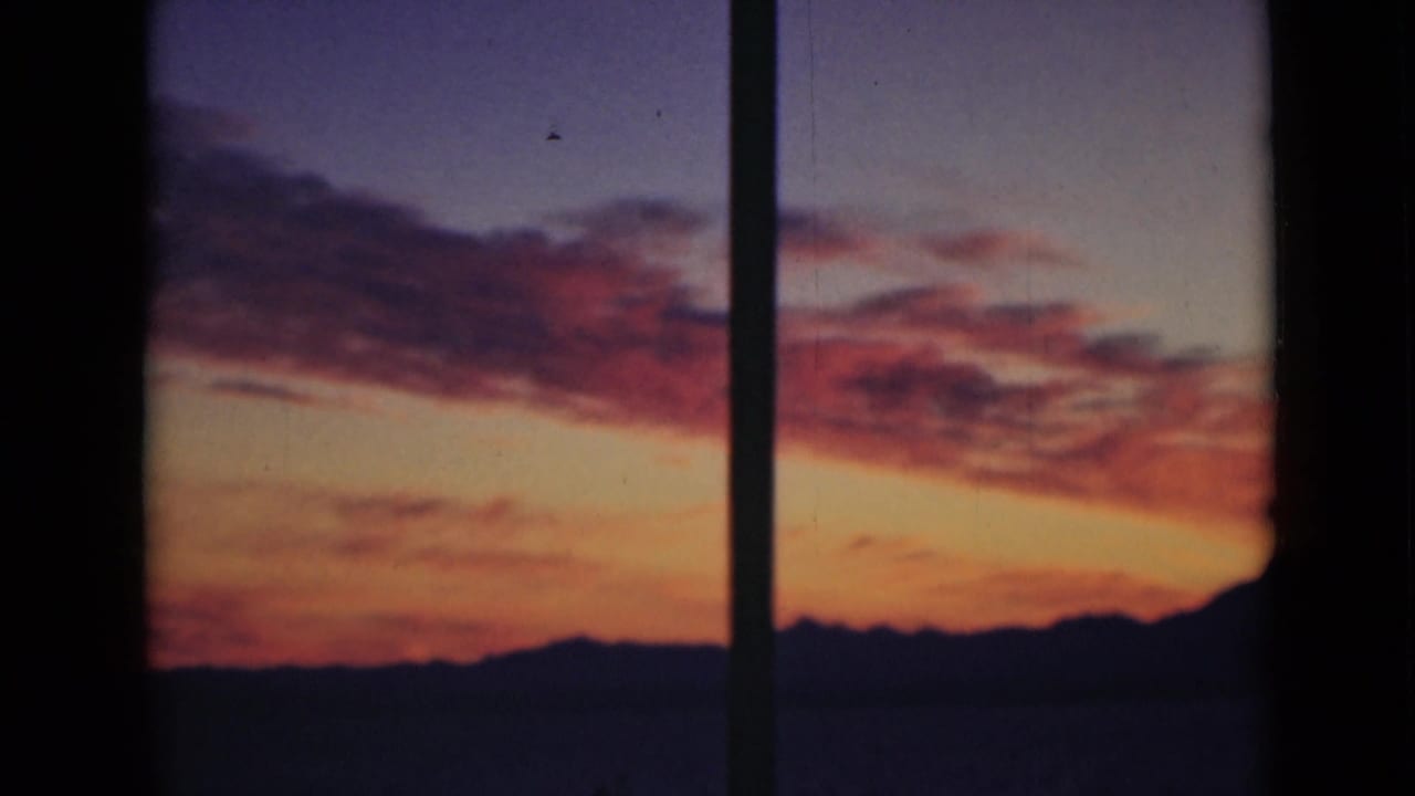 Orange and purple sunset sky over a dark horizon, divided by a vertical pole.