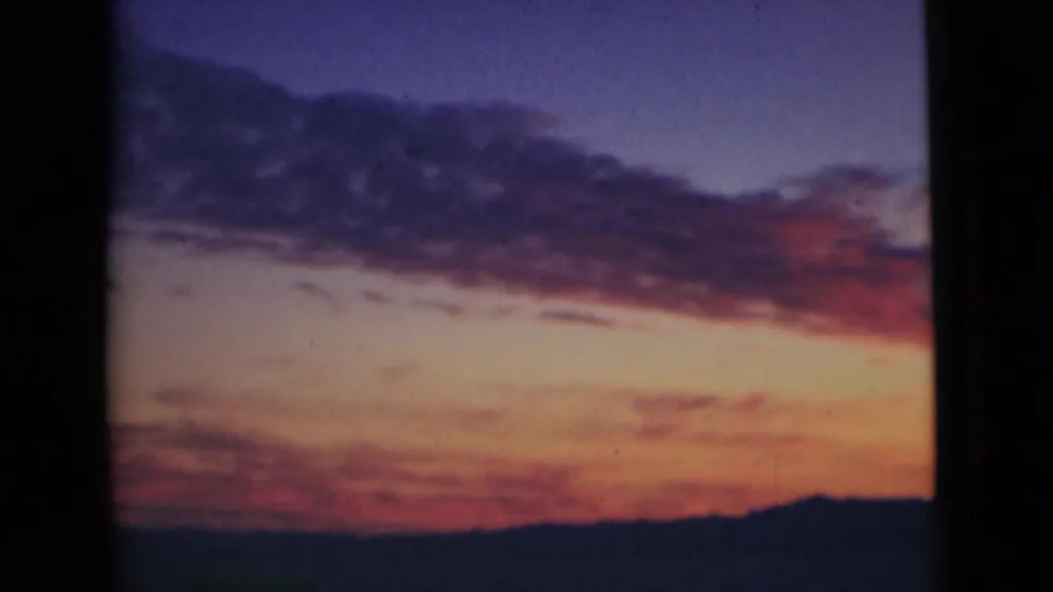 Final 8mm frame of the sunset, with purple-blue sky, reddish clouds, a dark low horizon, and a foreground vertical bar on the left.