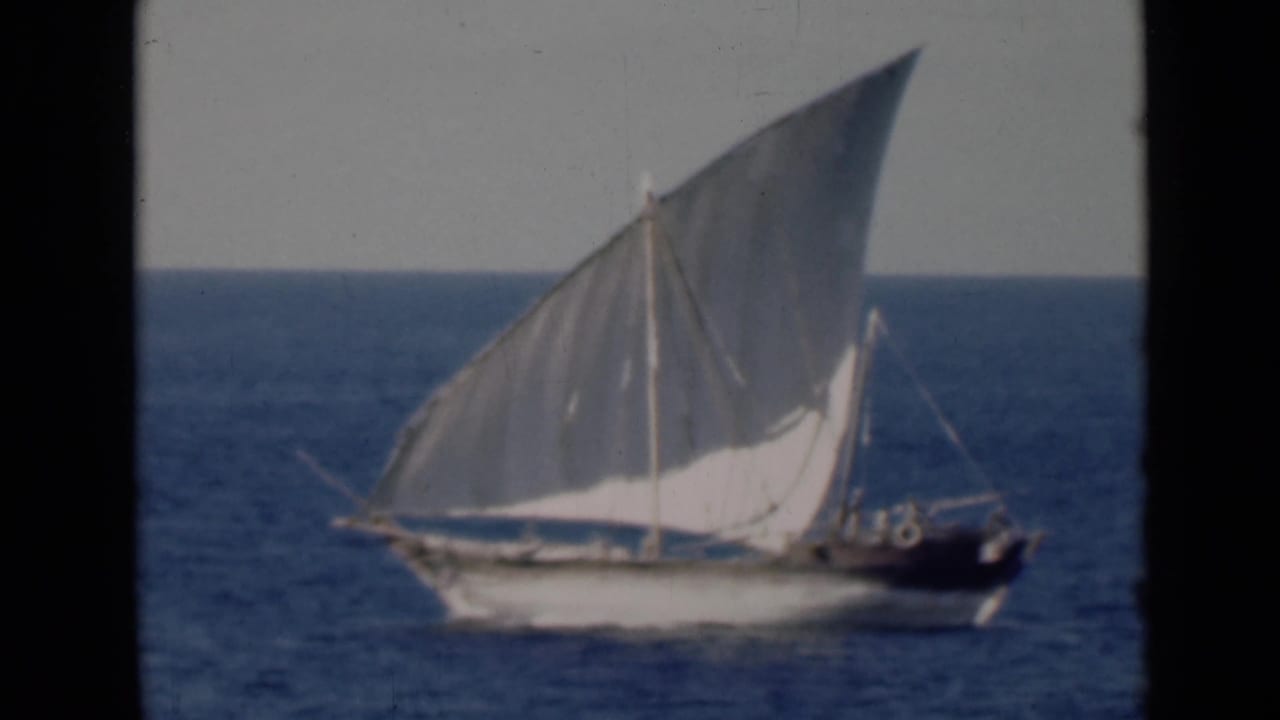 Traditional dhow sailing on blue water beneath a pale sky.