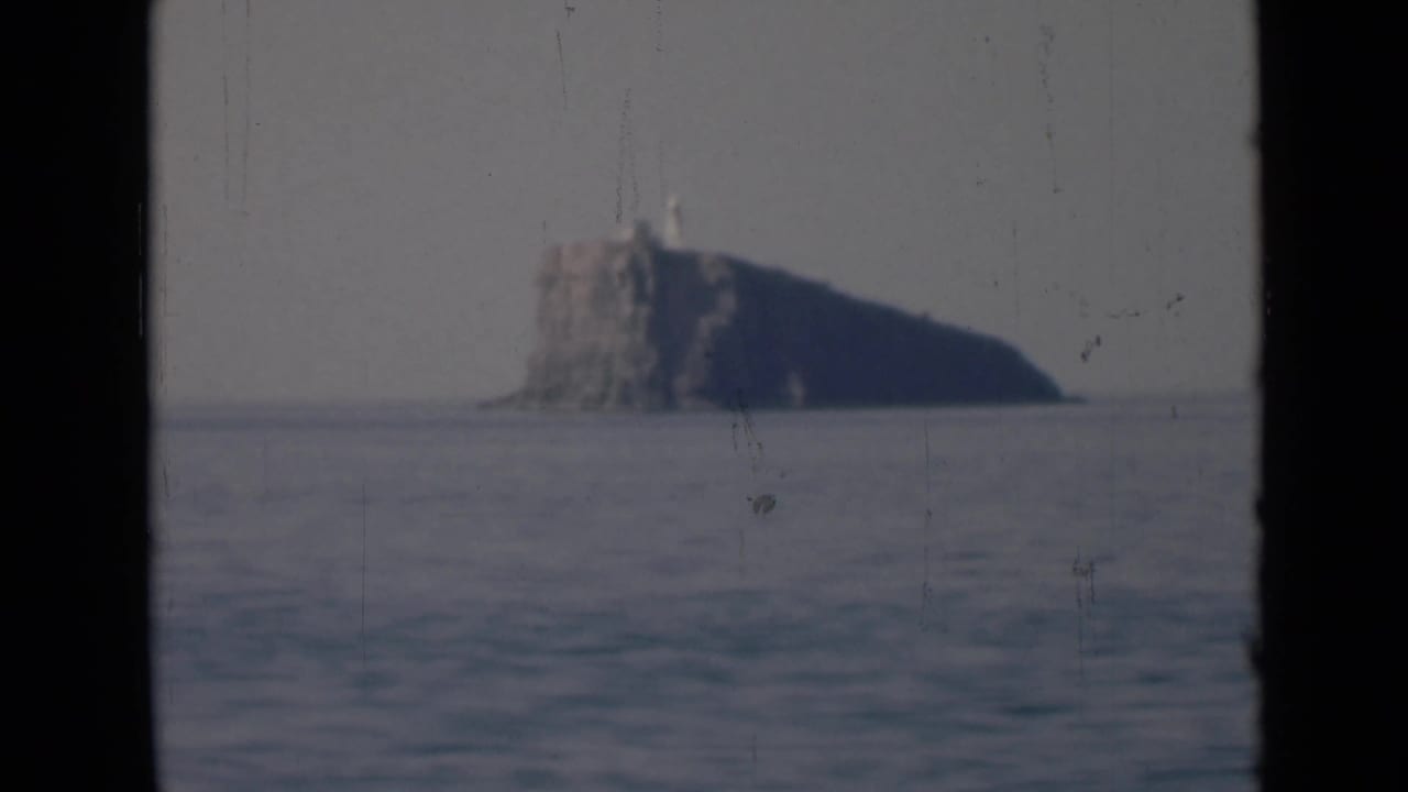 Distant rocky island with a small lighthouse-like structure across calm sea.