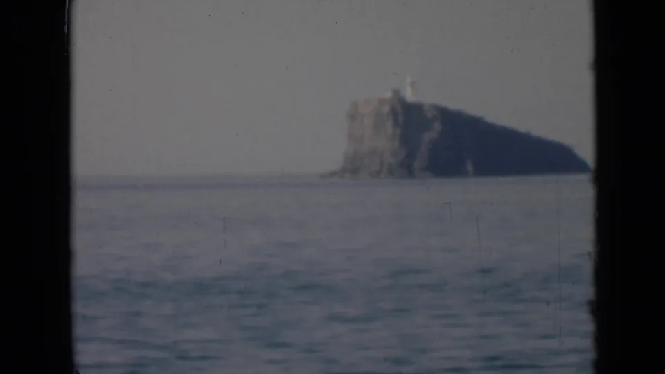 The final frame holds a distant rocky island with a lighthouse-like structure near the horizon under a pale, hazy sky.