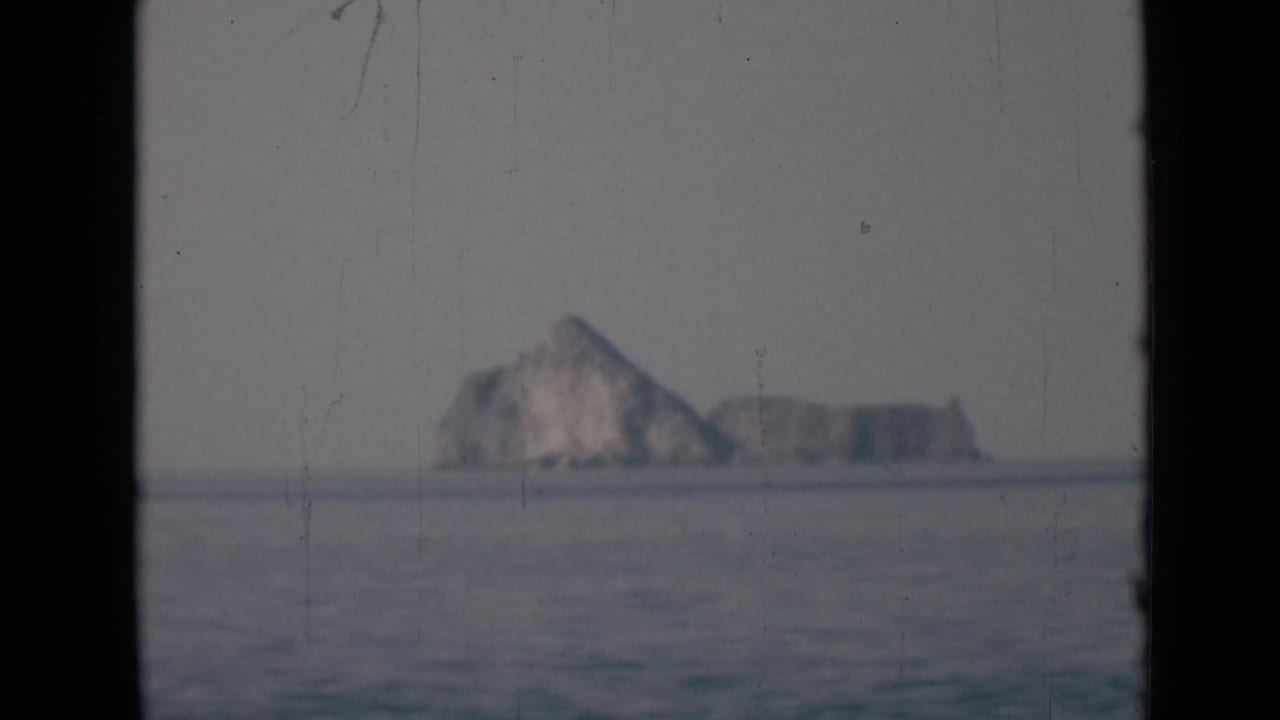 Distant rocky island across calm water, framed by dark film edges.