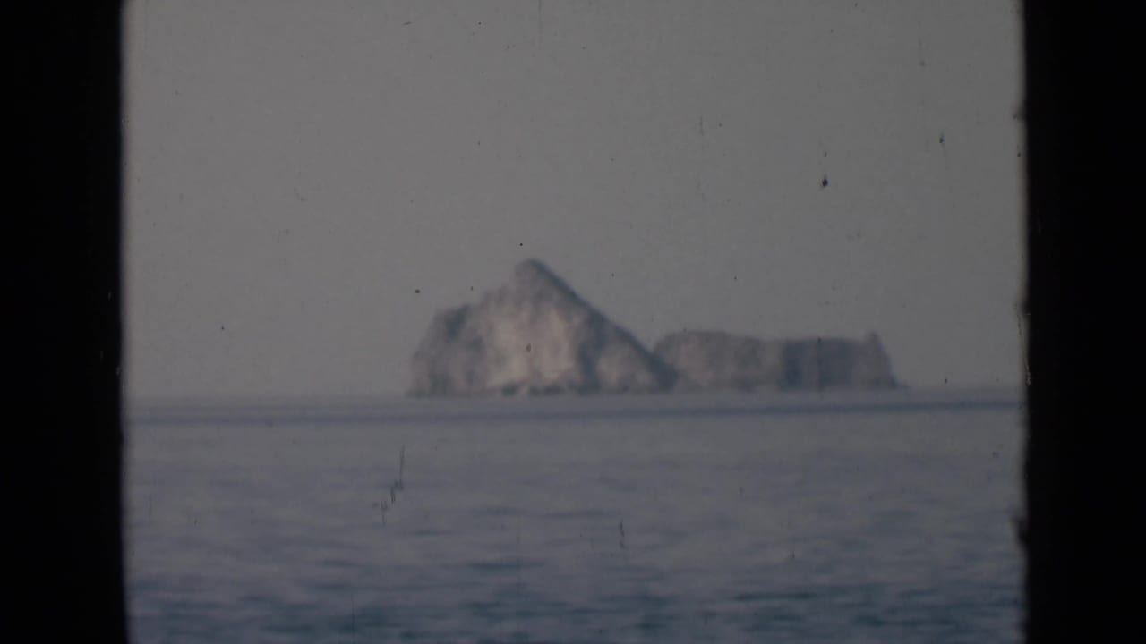 Distant rocky formation viewed across rippled water, with soft focus and vertical dark borders from the film frame.