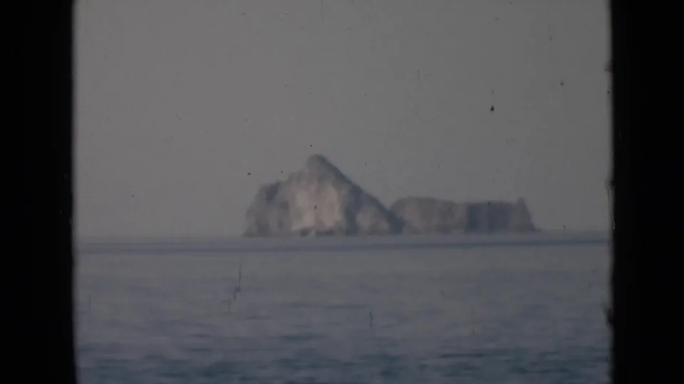 Distant rocky formation viewed across rippled water, with soft focus and vertical dark borders from the film frame.