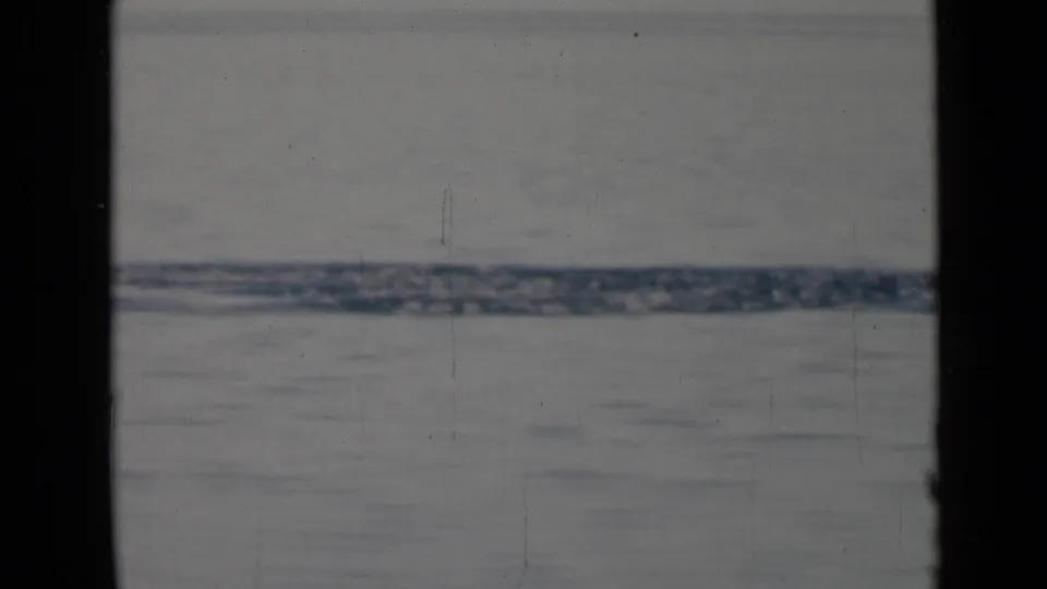1940s 8mm home-movie frame showing calm water and a distant hazy shoreline through a dark vessel window frame.