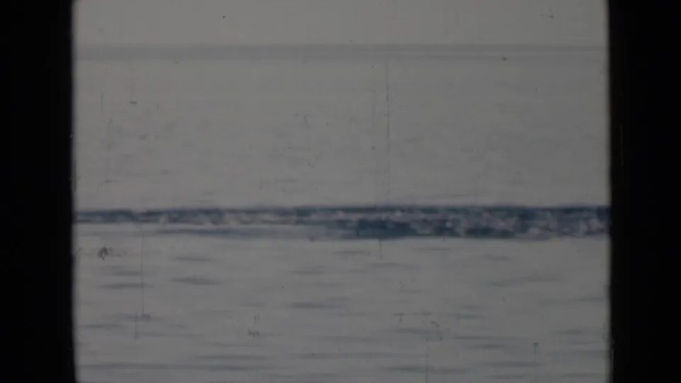 Vintage 8mm frame with calm water, a blurred coastal horizon, and dark vertical window framing from a vessel viewpoint.