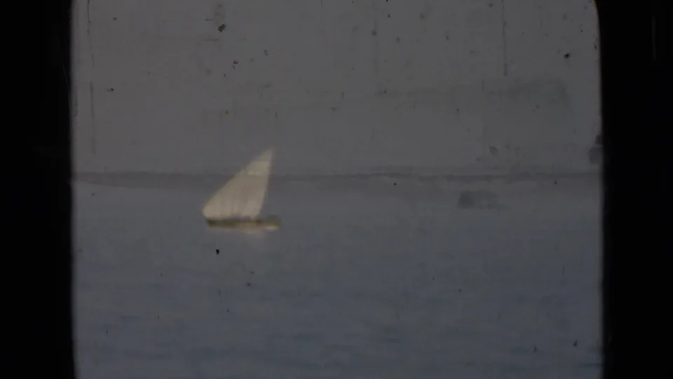 1940s Persian Gulf-labeled home-movie frame showing a small distant sailboat on calm water through a vessel window.