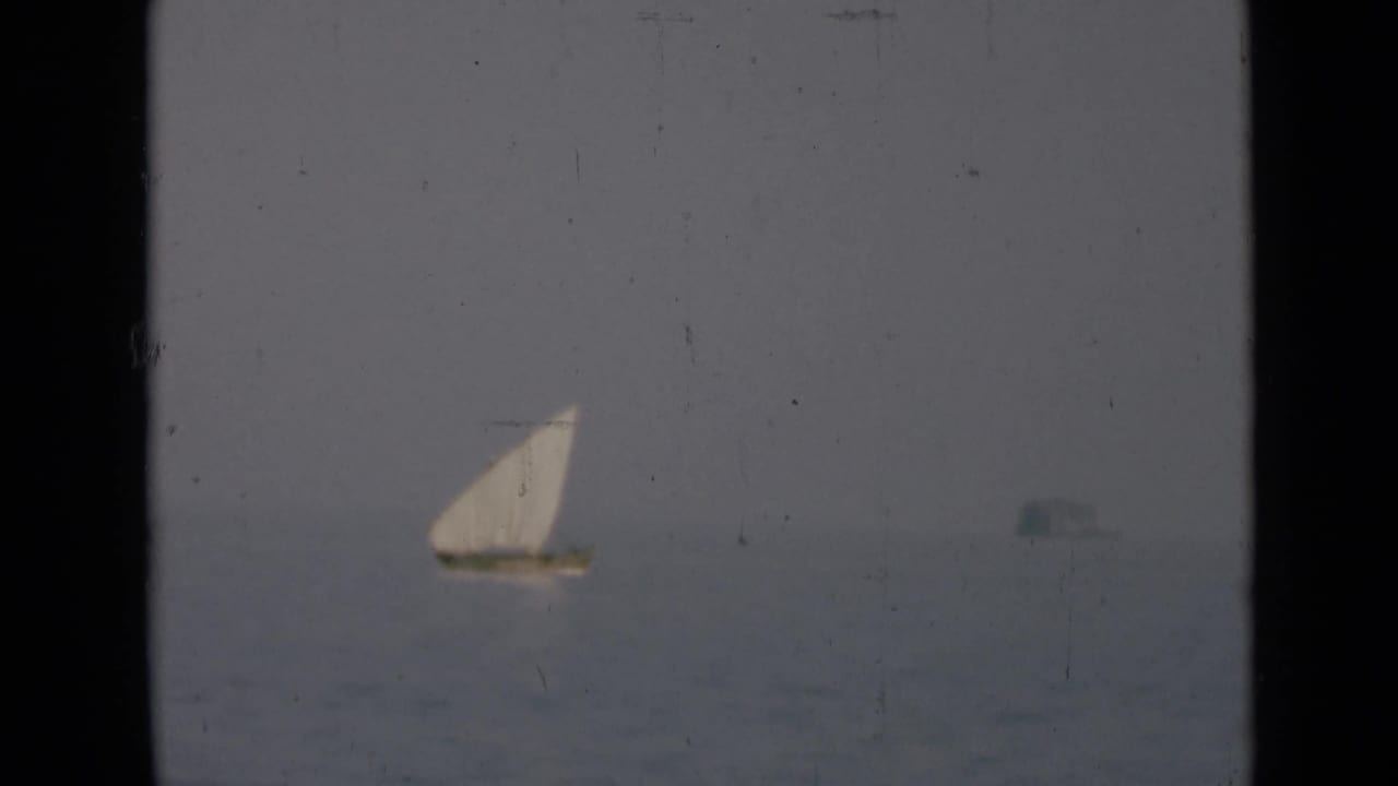 Distant sailboat on calm water with a faint shape near the horizon.