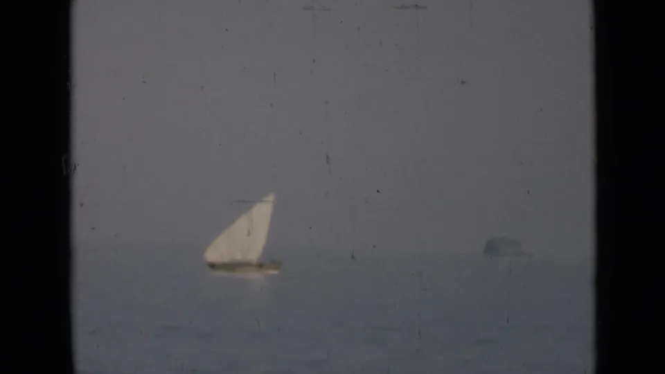 A small white-sailed boat is seen in soft focus on open water, with a faint distant shape near the horizon.
