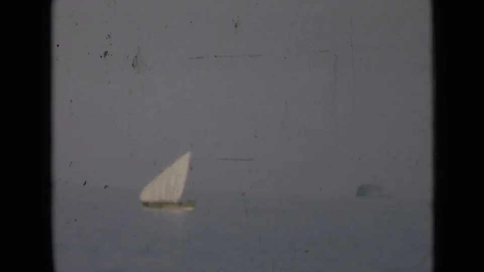 The sailboat sits low in the frame on calm water, with 8mm scratches and soft exposure visible across the scene.