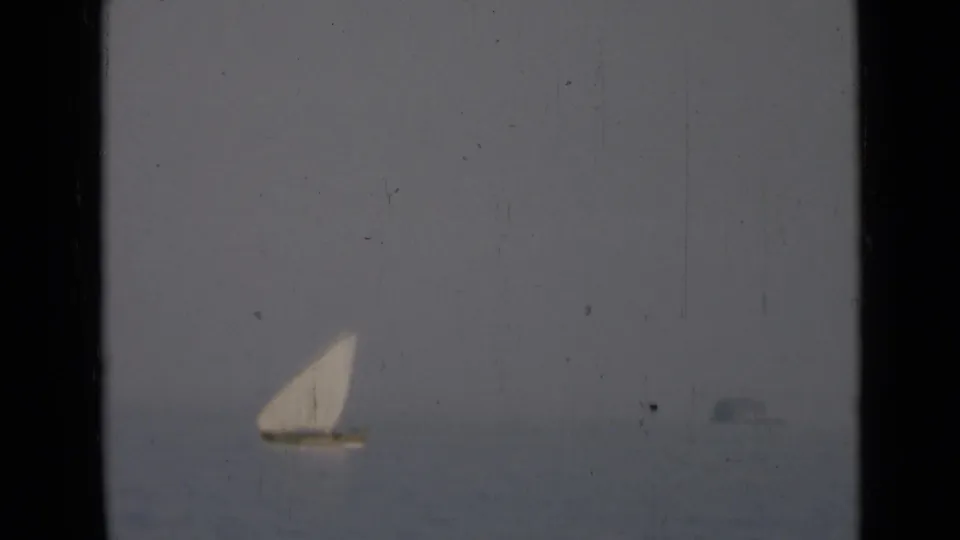 A distant white-sailed boat crosses calm water in a soft, scratched 8mm frame with no visible people or shoreline.