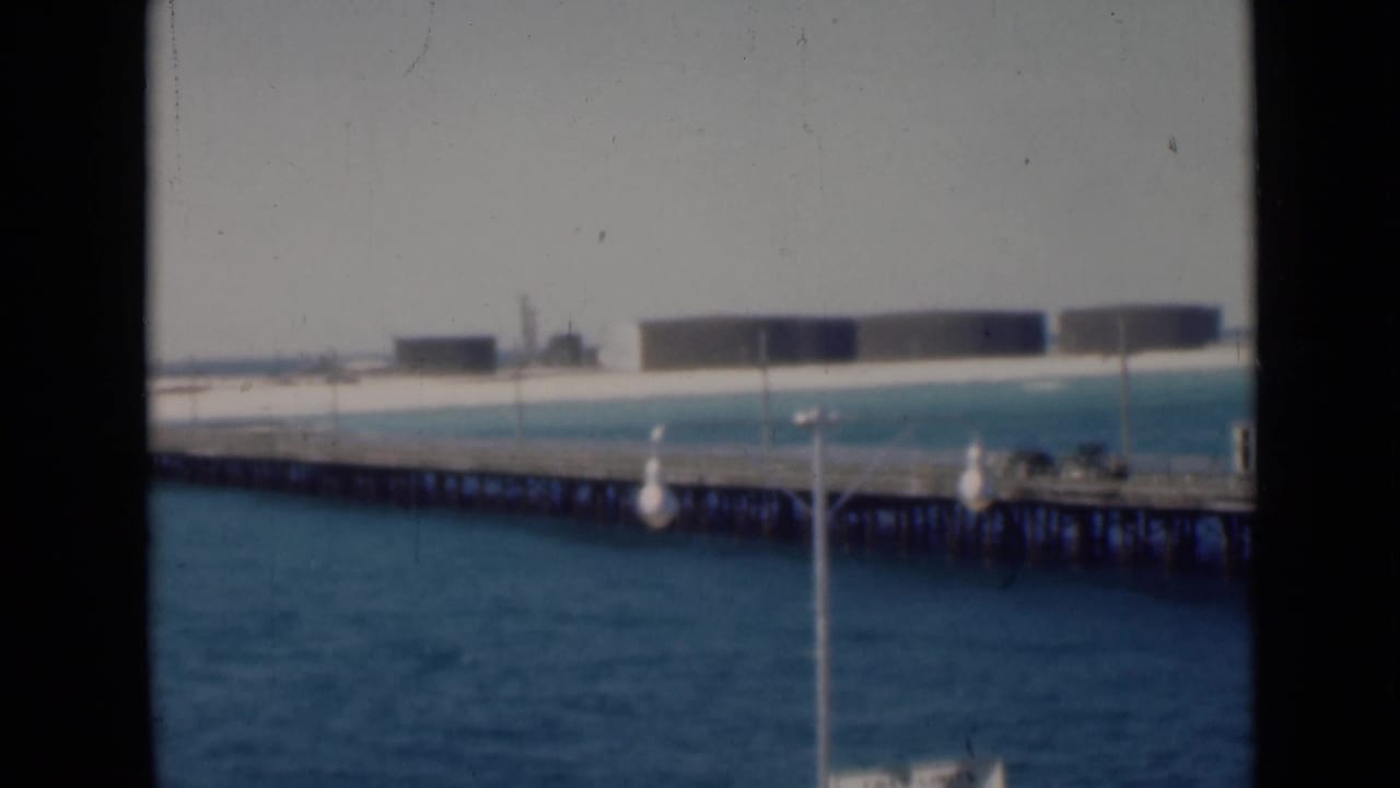 Pier and shoreline seen through dark vertical window frames, with blue water in front.