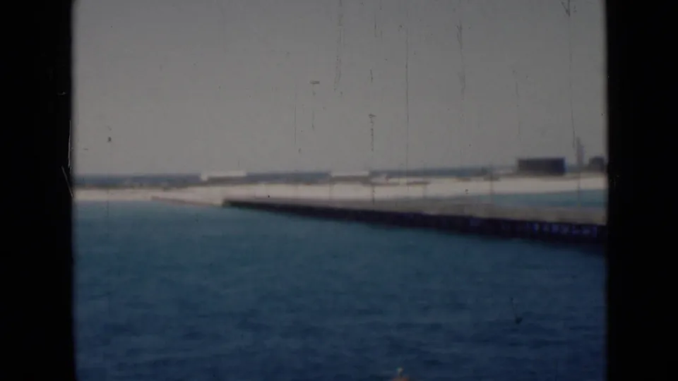Final frame shows open water and a long pier receding toward a pale shoreline, with sparse distant structures visible.