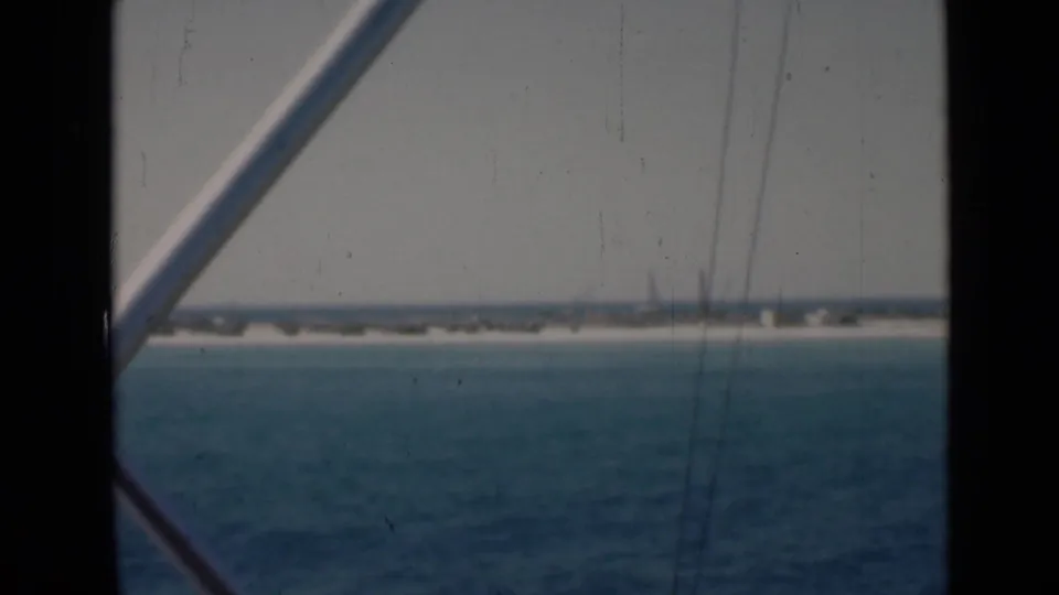 Soft 8mm frame with a diagonal boat railing crossing a turquoise-water view toward low shoreline.