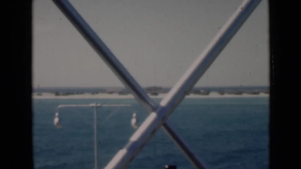 Persian Gulf water and a low shoreline appear behind a dark vertical post, white steel bracing, and a small waterfront light pole.