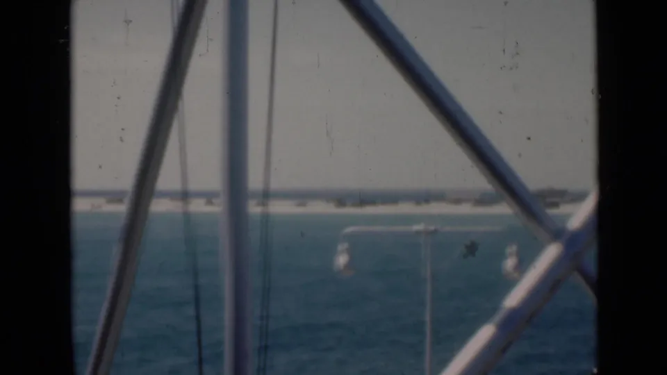 The final frame shows muted blue water and a low Persian Gulf shoreline through white diagonal beams, vertical supports, and visible film wear.