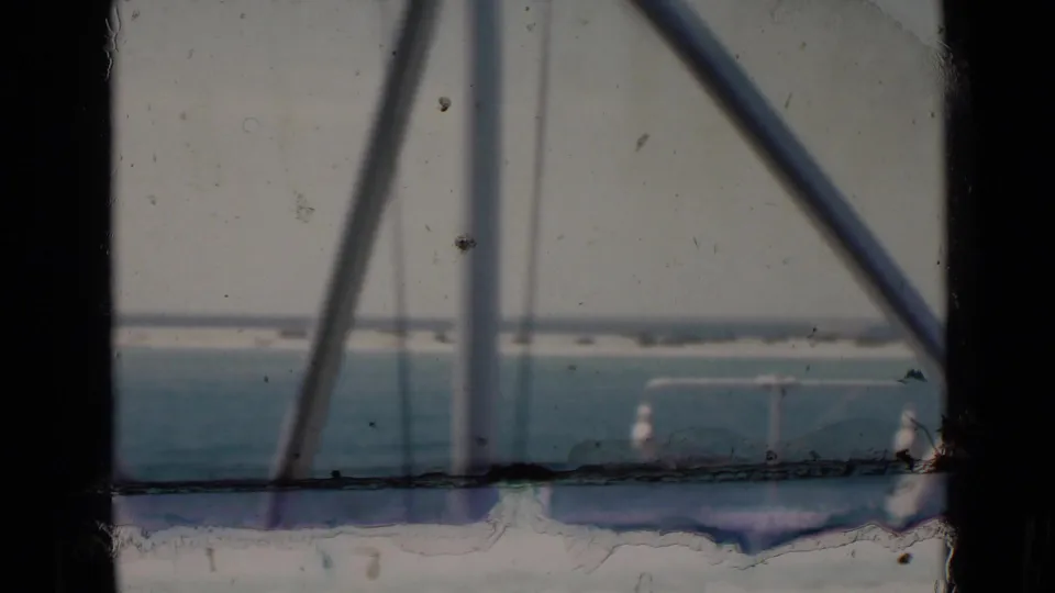1947 8mm home-movie view toward Persian Gulf water and a far shoreline, partly obscured by dark window edges and diagonal framing.