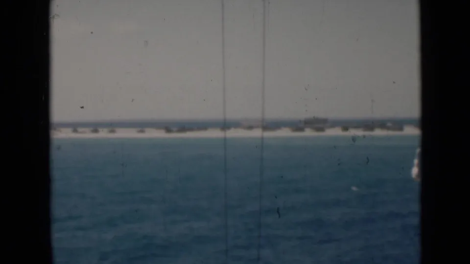 Soft 8mm view of Persian Gulf water with a pale low shoreline on the horizon, framed by dark vertical window or structural edges.