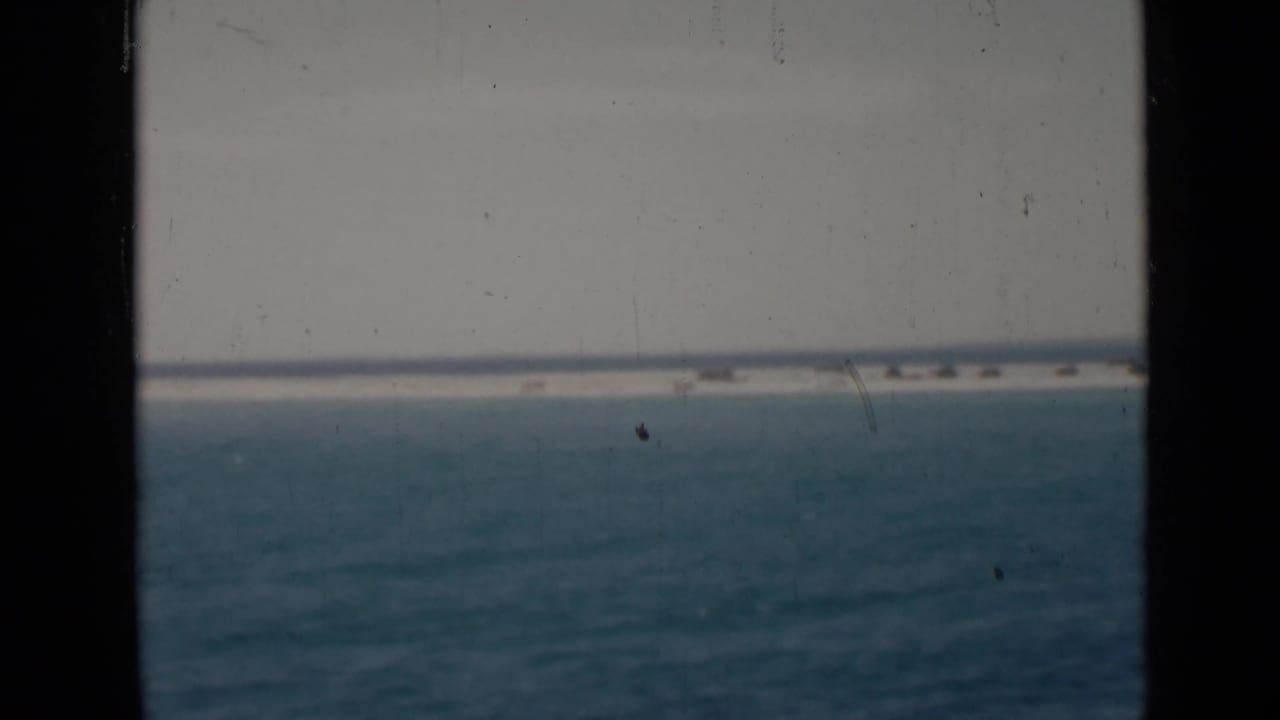 Open sea with a pale horizon and low sandbar, partly divided by a dark vertical frame strip.