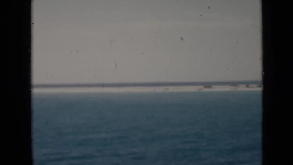 A moving-vessel view shows blue water, a pale sky, and a distant shoreline within dark 8mm frame borders.