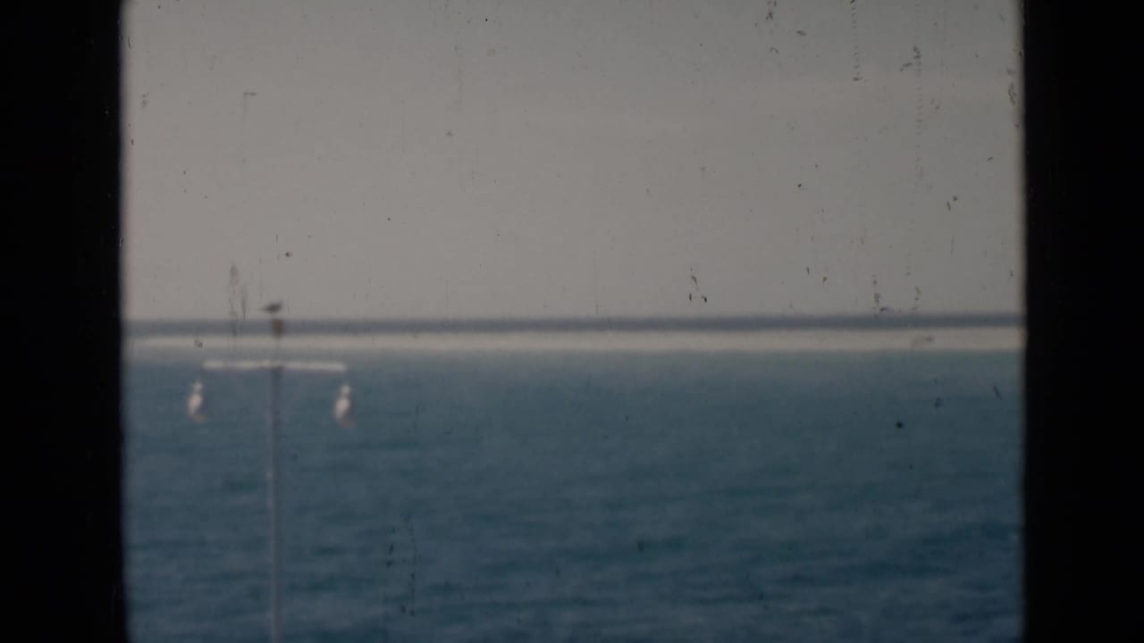 Blue ocean horizon seen through dark vertical frame edges with faint lamp posts in the distance.