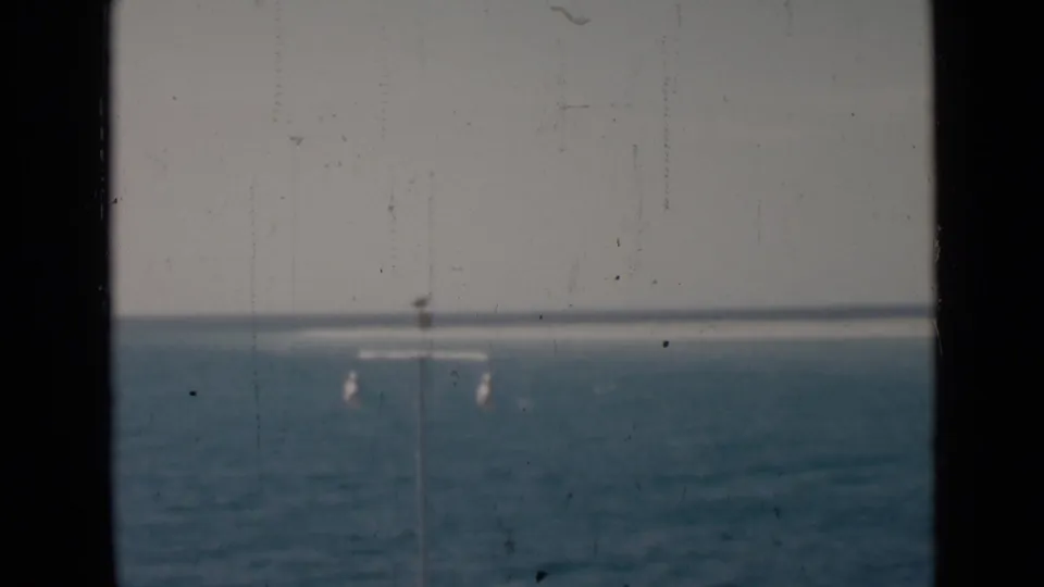 Soft 8mm frame showing Persian Gulf water, pale sky, and distant pier lamps split by a dark vertical divider.