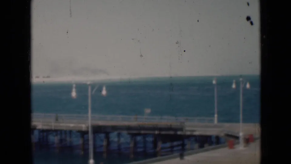 1947 8mm coastal view with pier decking, lamp posts, blue water, and hazy shoreline in the Persian Gulf region.