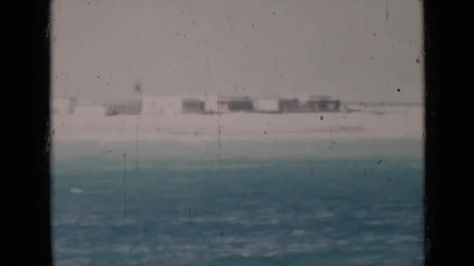 Soft 1947 8mm frame showing Persian Gulf water with faint shoreline structures beyond the bay.