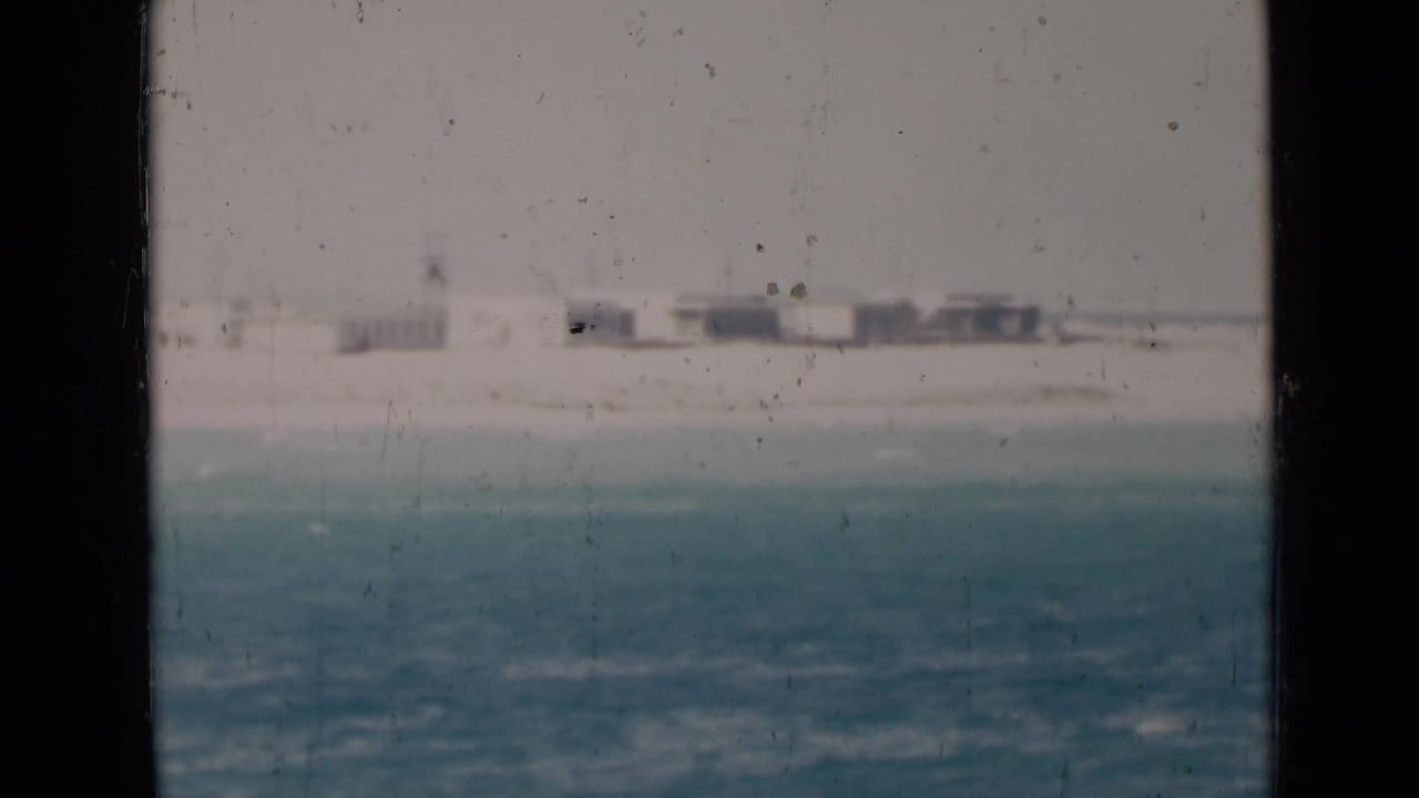 Distant sandy shoreline with low buildings beyond turquoise water.